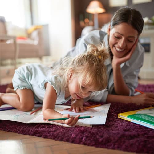Jeune femme souriante allongée au sol avec une petite fille qui dessine