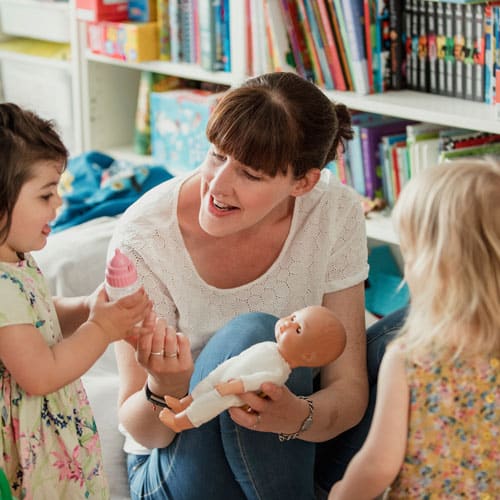 femme qui joue à la poupée avec deux petites filles