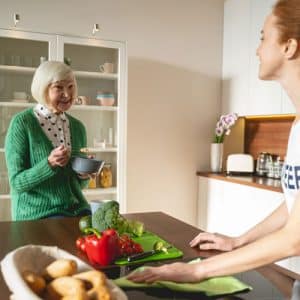 Jeune femme qui discute avec une femme âgée tout en nettoyant le plan de travail