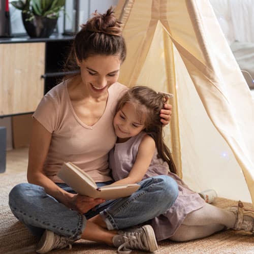 Jeune femme faisant la lecture à une petite fille, assises à coté d'une cabane