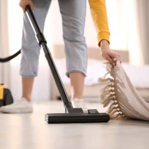 Femme qui soulève un tapis d'une main et qui passe l'aspirateur de l'autre