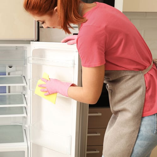 Femme qui nettoie la vitre d'un réfrigérateur