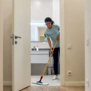 Jeune femme passant la serpillère tout en souriant dans une salle de bain