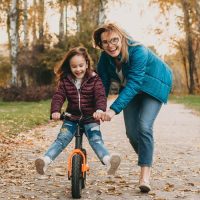 femme souriante apprenant à une petite fille à rouler à vélo